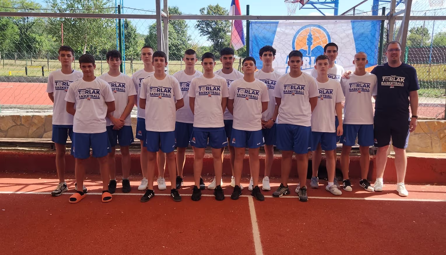 Basketball team of teenage boys and coach posing on an outdoor court in matching uniforms.
