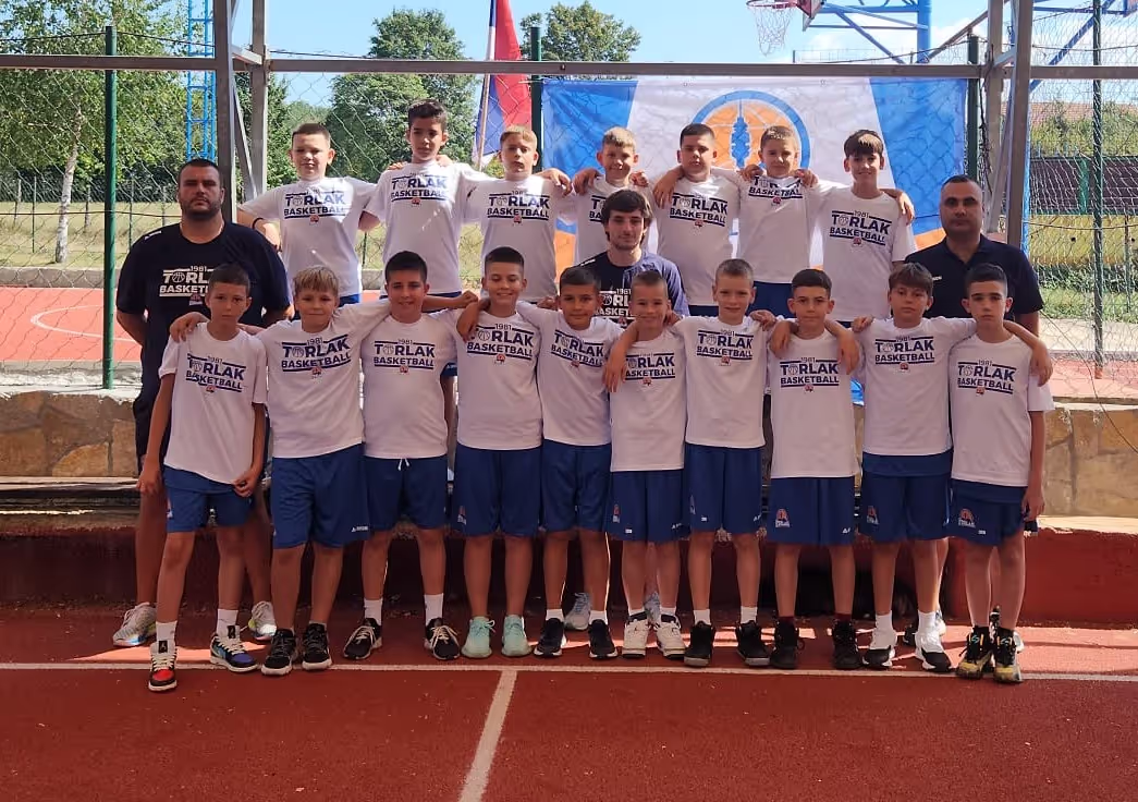 Youth basketball team in white T-shirts and blue shorts posing on outdoor court with coaches.