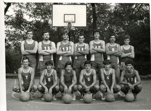 Black-and-white photo of a men's basketball team posing on an outdoor court with a hoop.