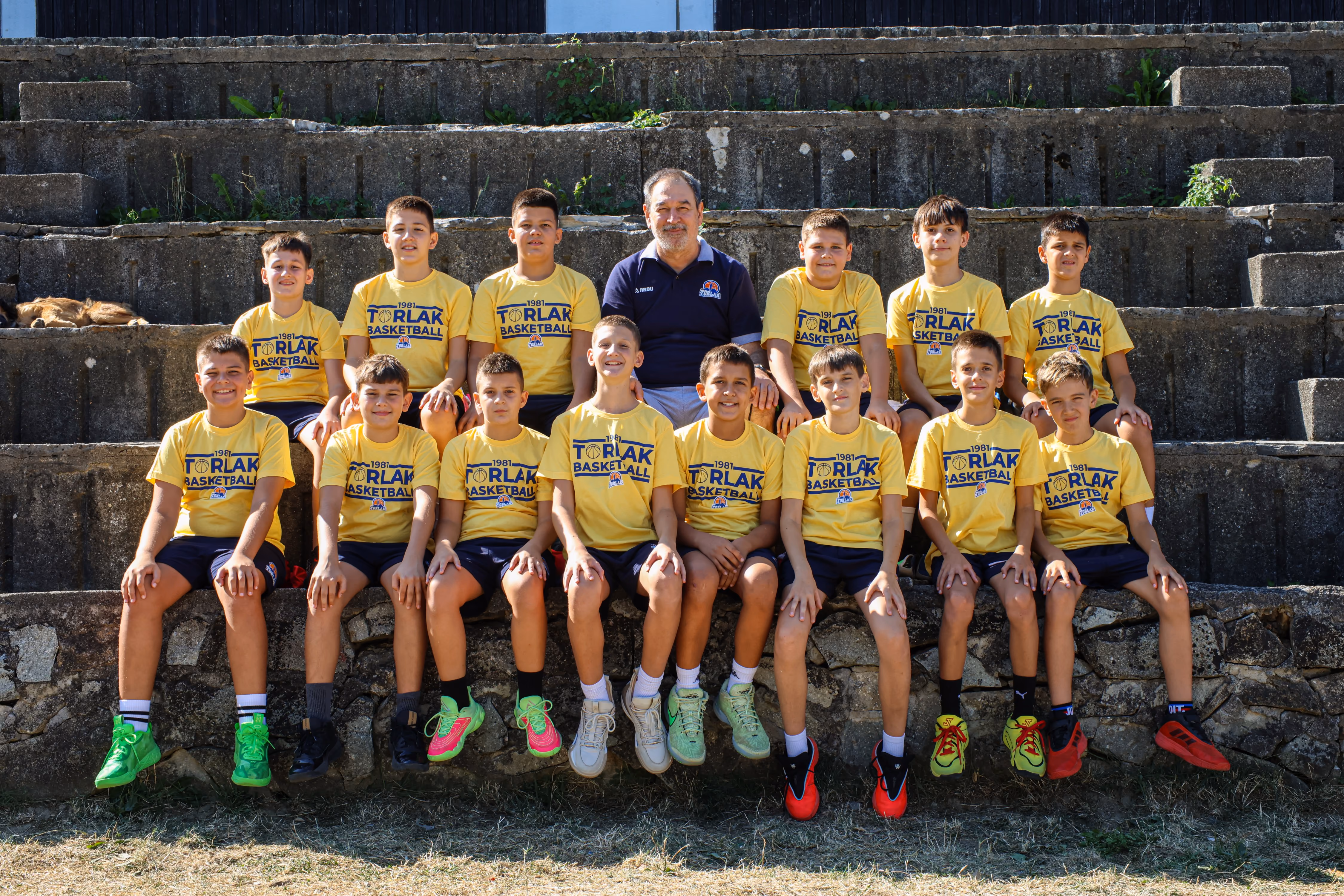 Youth basketball team posing in two rows on outdoor court wearing white Torlak Basketball shirts.